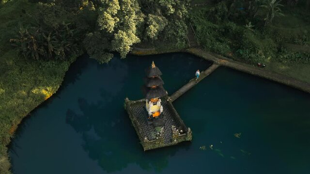 Woman visiting ancient holy temple in blue pond in tropical Bali, aerial
