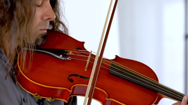 Close up profile of hispanic male musician with long hair and goatee playing red viola