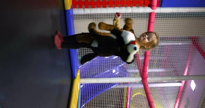 delighted toddler baby girl jumping on trampoline with puppy dog toy, having fun in play center. leisure activity in the amusement park