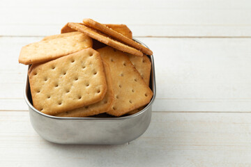 Cracker cookies in a stainless steel bowl on white wooden table background.