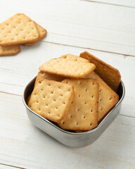 Cracker cookies in a stainless steel bowl on white wooden table background.