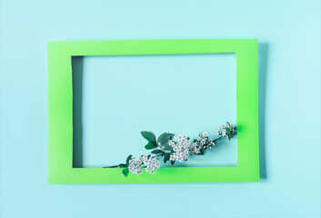 Green paper frame decorated with white flowers with green leaves on a light background of the apartment. Flat cardboard frame and decor of flowers and leaves