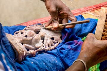Close-up view of a small sandstone religious statue being carved by the hands of a skilled Indian...
