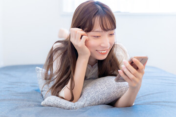 寝ながら笑顔でスマホを見る女性