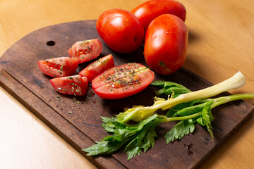Tabla con tomates orgánicos frescos cortados con orégano y aceite y, ramas pequeñas de apio