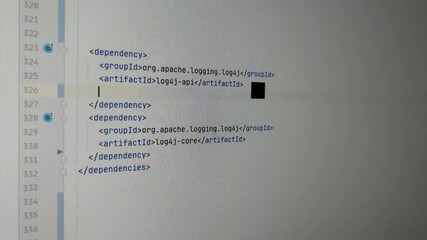 Programmer fixing zero day exploit Log4J bug with latest version. He is entering configuration lines in IDE software to set the version of the dependecy. Camera showing the monitor.