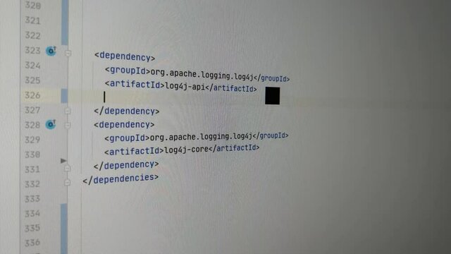 Programmer fixing zero day exploit Log4J bug with latest version. He is entering configuration lines in IDE software to set the version of the dependecy. Camera showing the monitor.