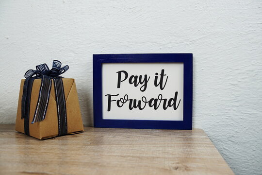 Pay It Forward Text And Gift Box On Wooden Table And White Wall Background