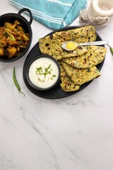 A Food called Methi paratha or Methi thepla is an Indian breakfast dish served with curd and a spoon full of desi ghee. with copy space. Indian fenugreek flatbread. Healthy lunch or dinner.