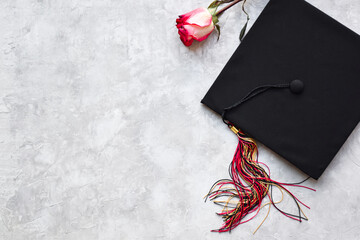 Graduation cap with a rose on grey background with copy space