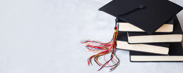 Graduation cap on stack of books on grey background web banner