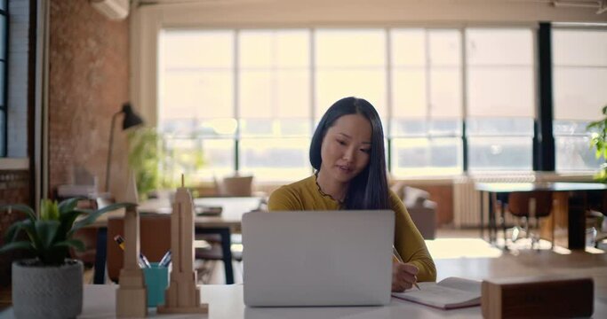 Attractive female business professional takes notes and writes in notebook in office desk working online frontal view