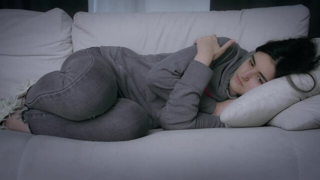 Sad girl lies on the couch hugging seba herself, depressed mood, the concept of parting and loss