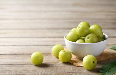 Fresh Amla (Indian gooseberry) fruits in white bowl on wooden table.