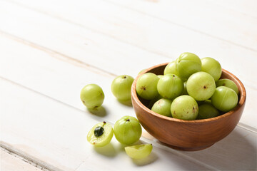 Fresh Amla (Indian gooseberry) fruits in wooden bowl on white wood.