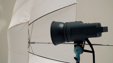 Big studio flashlight on a tripod and softbox paper in large size studio for video or film production.