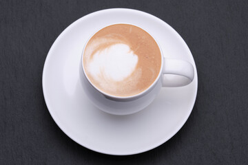 White cup of coffee with a saucer on a black background top view. Coffee with milk on black stones on top.