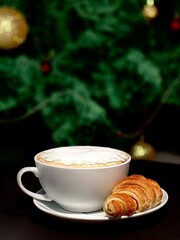a cup of coffee and croissant in the Christmas tree  background