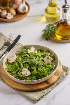 Arugula salad with shrimp and champignons, olive oil and dill on a wooden board on a white surface