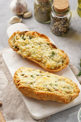 Two halves of garlic and butter bread - baguette on a marble board, sea salt, pepper, dill and garlic cloves on a grey concrete background, top view