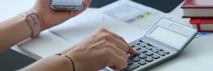 Woman looking at graph on mobile phone screen and counting on calculator closeup