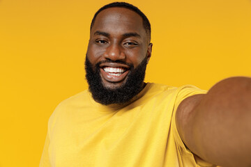 Close up young fun smiling happy black man 20s wearing bright casual t-shirt doing selfie shot pov on mobile phone isolated on plain yellow color background studio portrait. People lifestyle concept.