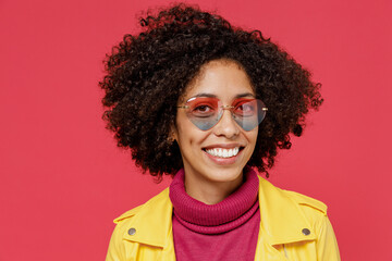Fancy bright happy young curly black latin woman 20s years old wear yellow jacket sunglasses looking camera smiling isolated on plain red background studio portrait. People emotions lifestyle concept