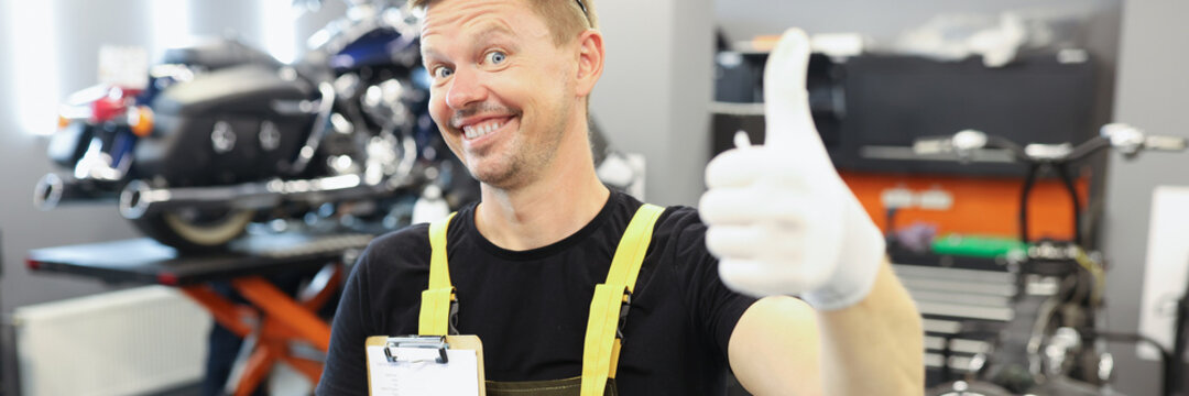 Auto mechanic showing thumb up and holding documents in repair shop