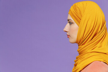 Side view severe sad young arabian asian muslim woman in abaya hijab yellow clothes isolated on plain pastel light violet background studio portrait. People uae middle eastern islam religious concept.