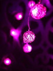 Magenta pink Rattan light balls garland on patterned wall. New Year's garland. Christmas led lights on dark background. Blurred glowing light bulb garland. Closeup. Vertical photo