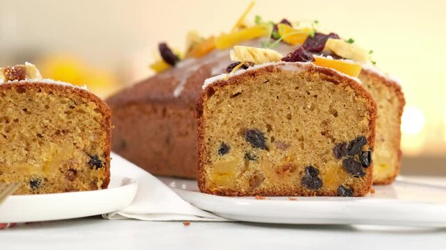 Close-up. A sliced fruitcake soaked in rum is on the table. Christmas atmosphere with lanterns in the background. Christmas homemade muffin. Traditional cupcake with dried fruits. Camera movement.