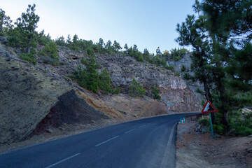 A road leading through a cut mountain slope made up of geological layers.