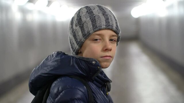 Portrait of alone confident boy in hat and jacket in underground covered walkway in city at winter