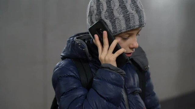 Portrait of a lonely confident boy in a hat and jacket talking on the phone in an underground covered passage in the city in winter