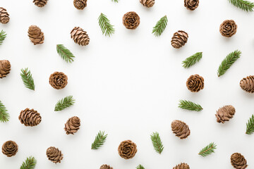 Round frame created from dry brown cones and green fir branches on white table background. Christmas natural decoration pattern. Empty place for inspirational wishes text, quote or sayings. Top view.