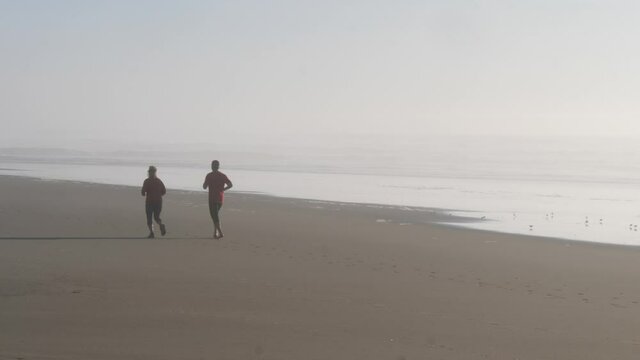 Two silhouettes of people runnning on a golden sand beach.