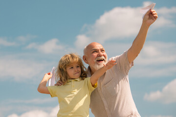 Grandfather and grandson with paper plane over blue sky and clouds. Men generation granddad and grandchild.