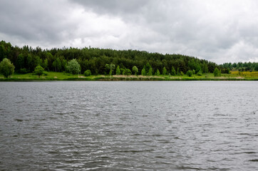 A view of a huge but shallow lake with a dense forest under a cloudy summer sky in the Russian countryside during a hike