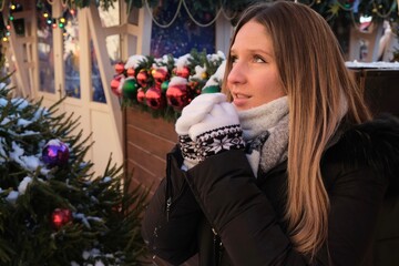 Portrait woman on traditional Christmas market. Xmas Presents Holidays concept. New Year's Fair. A woman warms her hands by rubbing in the cold