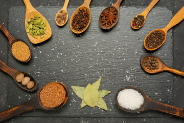Various herbs and spices in wooden spoons on slate board. Flat lay of spices ingredients pepper, anise star, nutmeg, allspice, clove, mustard seeds and cardamom on slate.