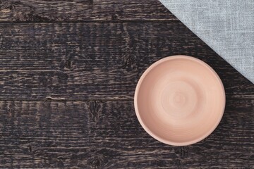 An empty bowl of white clay and a gray cloth napkin on an old wooden table surface. Flat lay