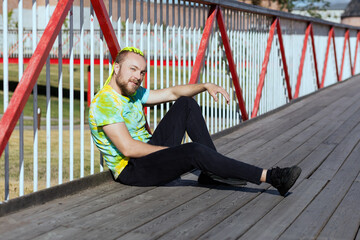 A man with an interesting mohawk hairstyle sits on the bridge and covers his eyes from the sun with...