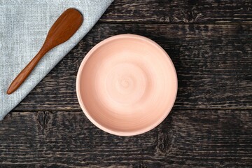 An empty white clay bowl and a wooden spoon on a gray cloth napkin on an old wooden table surface. Flat lay