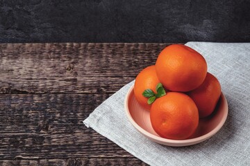 Tangerines in a white clay bowl on a gray cloth napkin on an old wooden table surface.