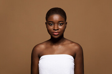 Minimalist Makeup. Attractive african american female wearing towel standing on brown background