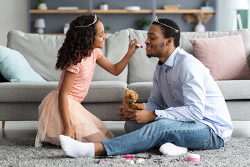 Pretty black girl daughter putting makeup on her father face