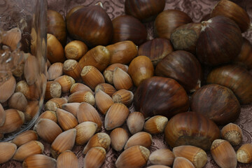 Obraz premium Many different nuts (chestnut, hazel, acorn) laid out on brown background, near a transparent glass, narrow depth of field, blurry bokeh