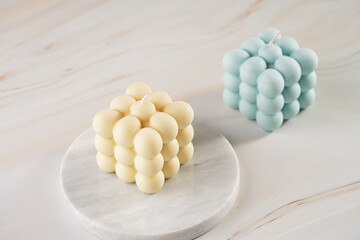 One white square bubble candle on a marble board and one blue on a tropical background