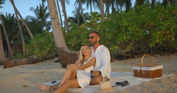 Lovely couple having picnic on evening sandy beach man hugs his girlfriend, enjoying time together