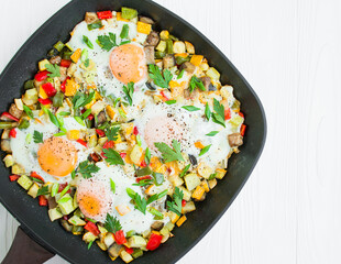 Fried eggs with vegetables in a square frying pan on a light table. Homemade shakshuka, top view.